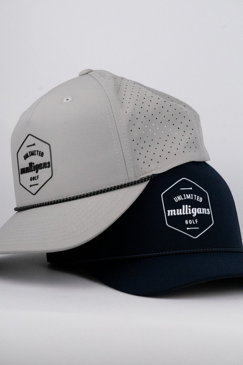 Two rope caps, one gray and one navy, with 'Unlimited Mulligans Golf' logo on a light gray background.